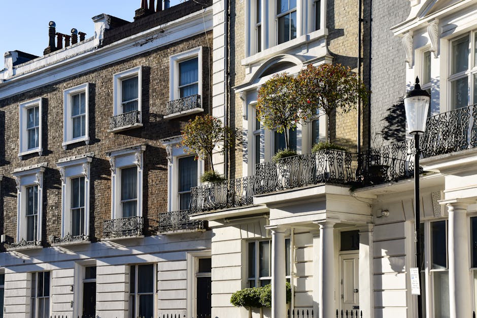 A row of elegant, multi-storey terraced houses in Brentford, featuring a mixture of brick and white-painted facades. Each property has tall, narrow windows with white trim, some with decorative black